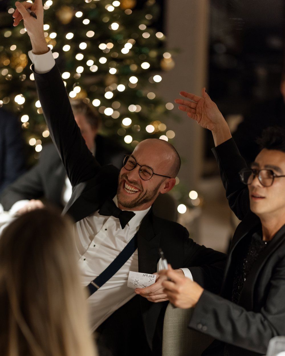 CreativeGrounds x Zoldering Christmas dinner: two guests in black tie raising their hands at the table