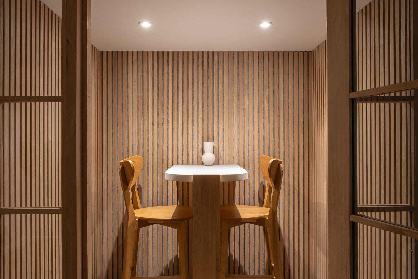 Phone booth at CreativeGrounds coworking, Amsterdam Oud-Zuid, lined with oak slats, with a small white table, two oak bar chairs and a white vase