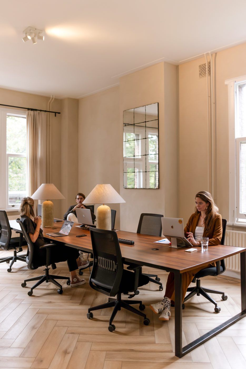Members working at a shared oak table with brass lamps in the CreativeGrounds coworking, Amsterdam Oud-Zuid