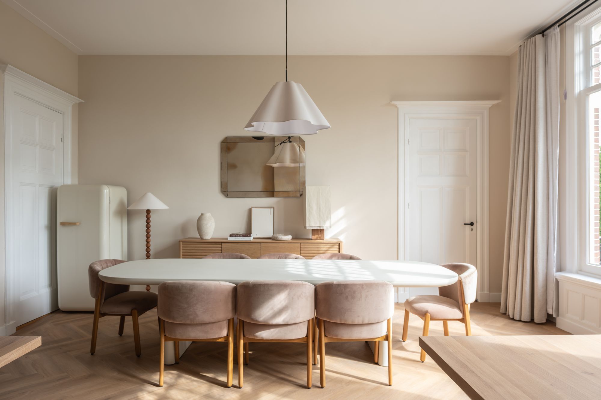 White oval meeting table with pink upholstered chairs under a pendant lamp inside a CreativeGrounds private office suite, Amsterdam Oud-Zuid