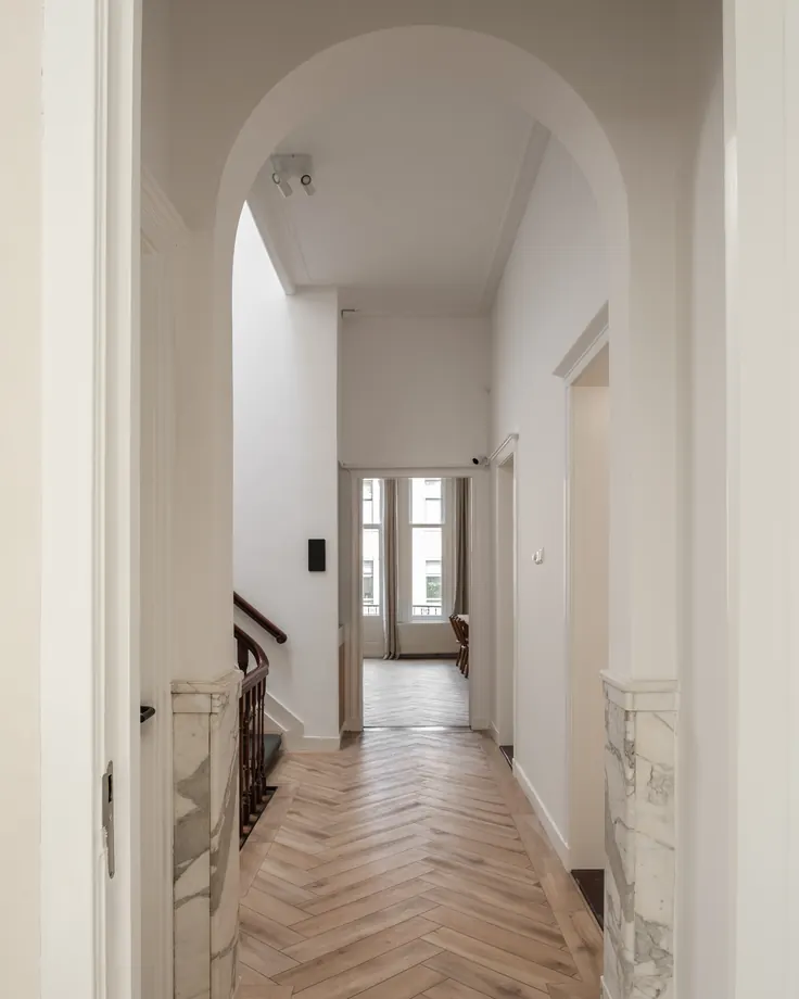 Hallway with a marble arch and herringbone floor, looking through to the front windows